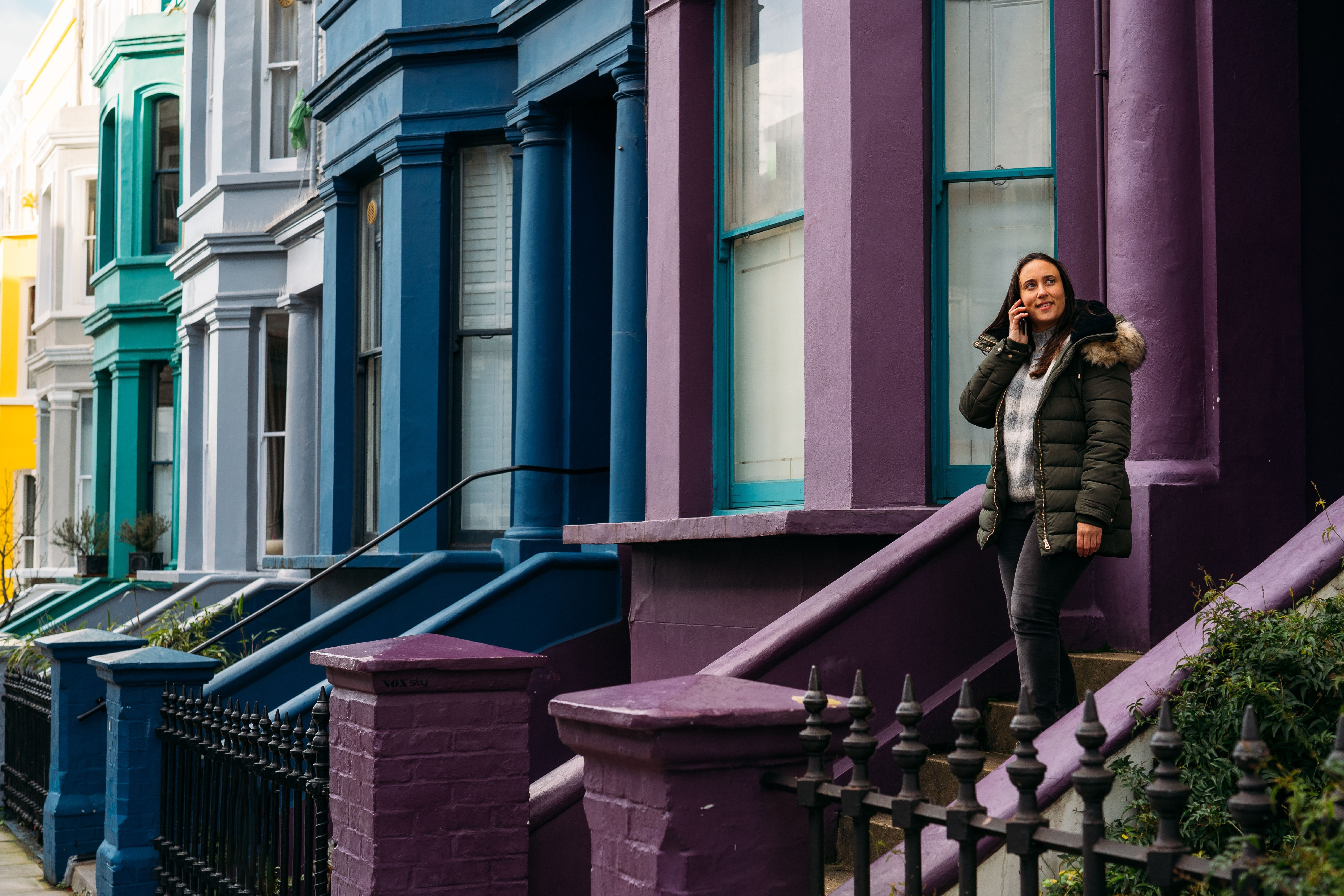 A woman walking out of a front door of a colourful row of terraced housing.